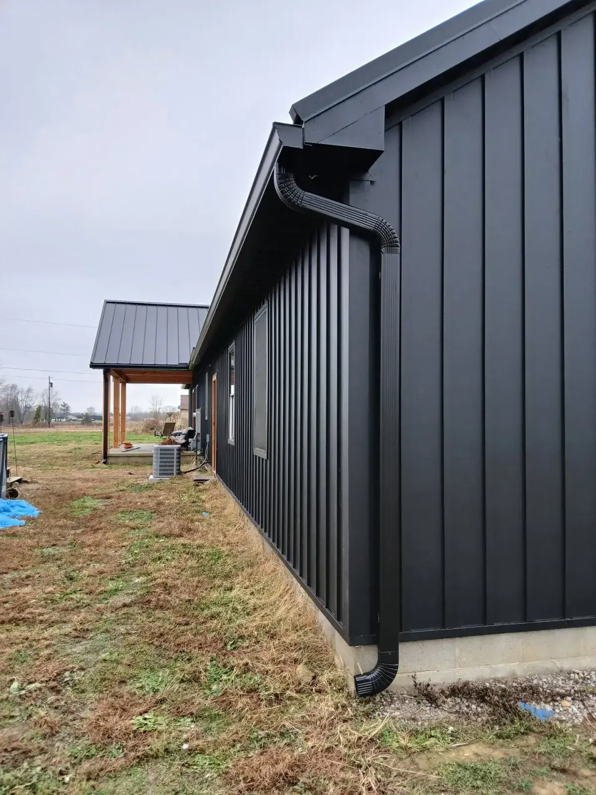 Black seamless gutter and downspout running down black board and batten metal siding