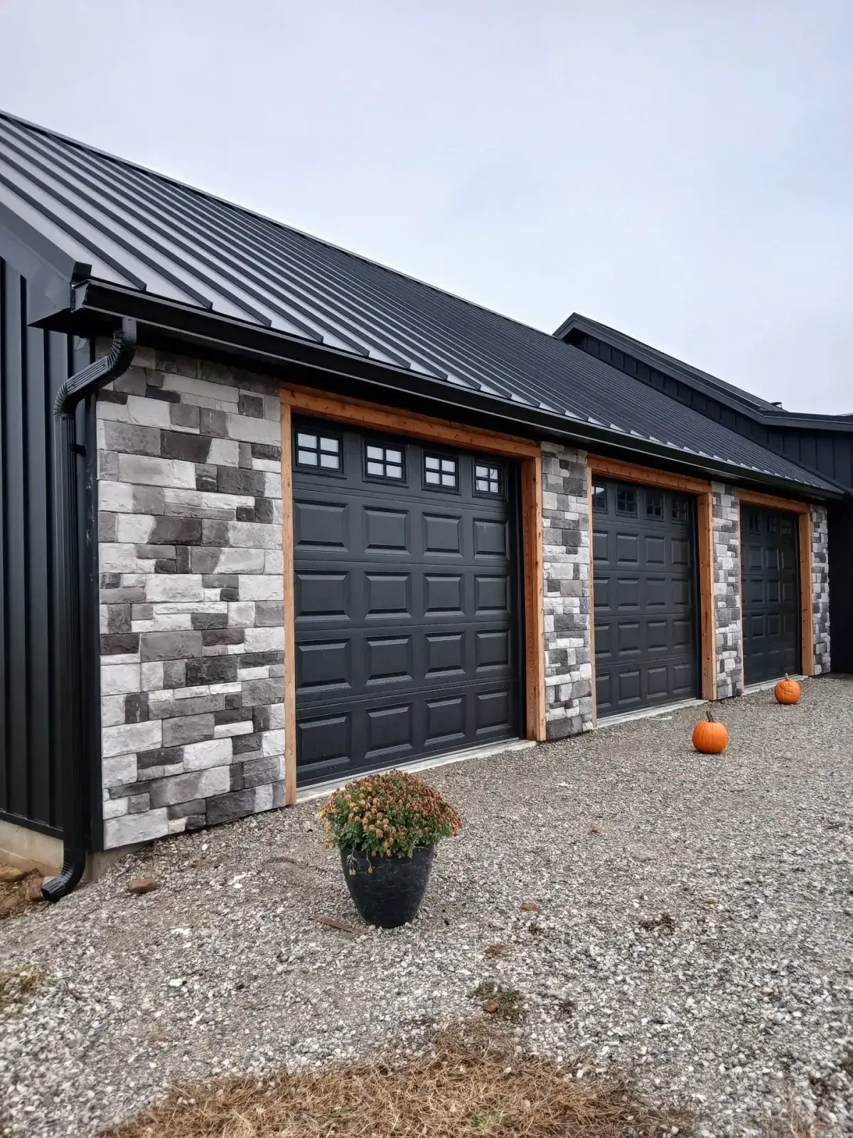 Black standing seam metal roof over a three-bay garage with stone columns and cedar trim